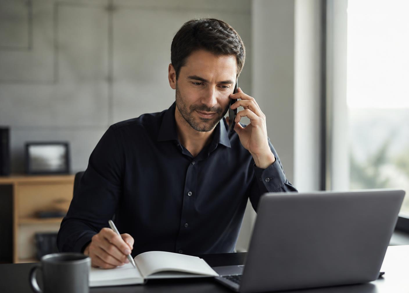 Sales manager taking notes on a customer call while reviewing the pipeline on a laptop