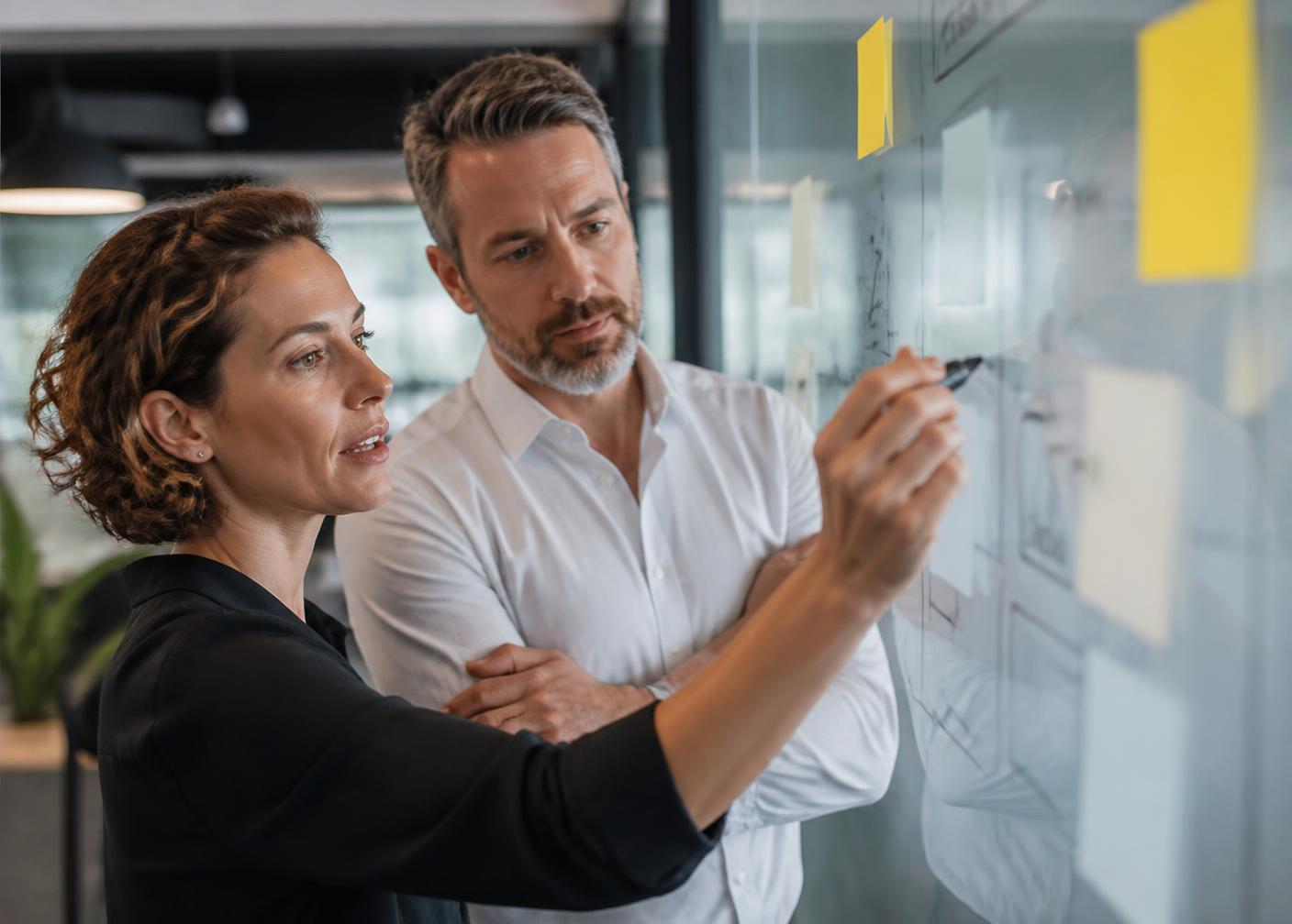 Two managers mapping a business workflow on a glass wall with notes and diagrams